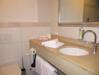 Ein modernes Badezimmer mit einem sauberen Waschbecken und einem großen Spiegel. Frische Handtücher und Toilettenpapier sind ordentlich auf dem Tisch platziert.