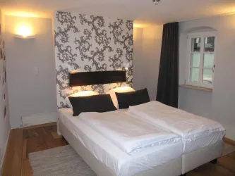 Ein modernes Schlafzimmer mit einem Doppelbett und eleganter Tapete. Das Zimmer hat ein Fenster und warme Beleuchtung.