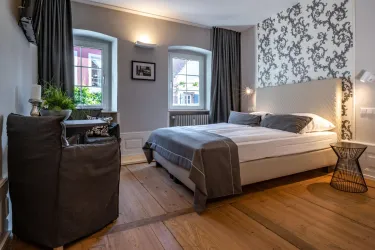 Ein modernes Schlafzimmer mit einem großen Bett und stilvollen Einrichtungselementen. Die Wände sind mit einem eleganten Muster geschmückt und es gibt viel Tageslicht durch die Fenster.