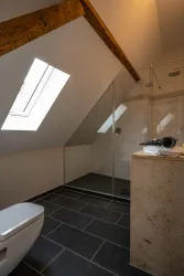 Ein modernes Badezimmer mit einer Duschkabine und großen Fenstern. Die Wände sind hell und die Böden sind dunkel gefliest.