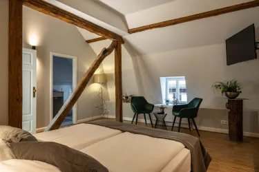 Ein stilvolles Schlafzimmer mit Holzdeckenbalken und zwei Einzelbetten. Im Hintergrund befinden sich ein Fernseher und ein kleiner Tisch mit Stühlen.