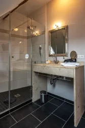 Ein modernes Badezimmer mit einer gläsernen Dusche und einem eleganten Waschtisch. Die Wände sind hell, und der Boden ist mit dunklen Fliesen gestaltet.