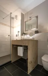 Ein modernes Badezimmer mit einer Dusche und einem eleganten Waschbecken aus Stein. Die Wände sind hell gefliest und das Ambiente ist freundlich und einladend.