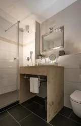 Ein modernes Badezimmer mit Dusche und stilvollem Waschbecken. Die Wände sind in einem neutralen Ton gehalten, und es gibt einen großen Spiegel.