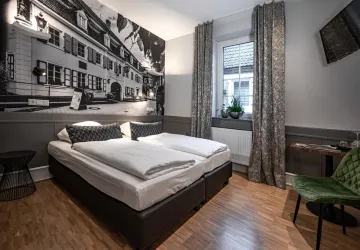 Ein modernes Hotelzimmer mit zwei Einzelbetten und einem großen Wandbild. Durch das Fenster fällt natürliches Licht, das den Raum gemütlich wirkt.
