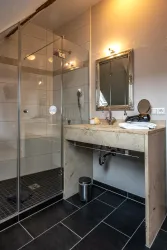 Ein modernes Badezimmer mit einer Dusche aus Glas und einem eleganten Waschbecken. Die Wände sind hell und der Boden ist mit dunklen Fliesen gestaltet.