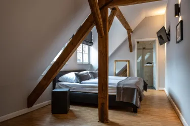 Ein modernes Schlafzimmer mit einem Doppelbett und Holzbalken. Es gibt einen Spiegel und einen Fernseher an der Wand.