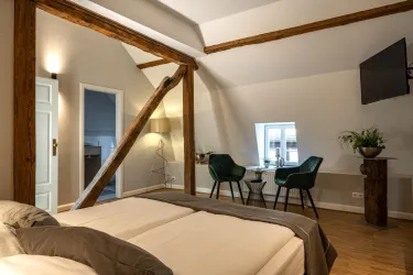 Ein modernes Schlafzimmer mit zwei Betten und Holzbalken. Es gibt einen kleinen Tisch mit Stühlen und einen Fernseher an der Wand.