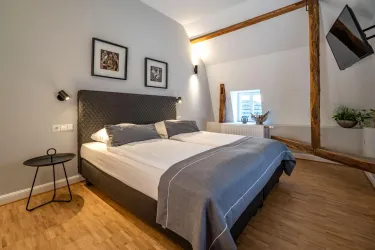 Ein modernes Schlafzimmer mit einem bequemen Doppelbett und Holzfußboden. An den Wänden hängen Bilder und es gibt eine kleine Sitzecke mit einem Tisch.
