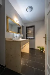 Ein modernes Badezimmer mit einem eleganten Waschtisch und einem großen Spiegel. Der Boden ist mit dunklen Fliesen ausgelegt und ein Fenster sorgt für natürliches Licht.