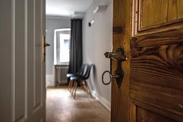 Ein Blick durch eine halb geöffnete Tür in einen modernen Raum. Im Hintergrund sieht man zwei schwarze Stühle und ein Fenster.