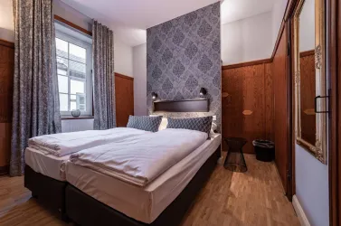 Ein gemütliches Schlafzimmer mit einem Doppelbett und stilvollen Vorhängen. Die Wände sind teilweise in einem eleganten Muster gestaltet.