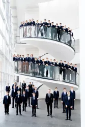 Eine Gruppe von Jungen in formeller Kleidung steht auf einer modernen Treppe. Die Szene hat eine helle, elegante Atmosphäre.