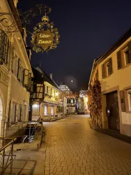 Eine ruhige Straße in einer historischen Stadt bei Nacht. Die Gebäude sind gut beleuchtet und erzeugen eine einladende Atmosphäre.