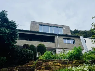 Ein modernes Haus mit großen Fenstern und holzverkleideter Fassade. Der Garten ist grün und gut gepflegt.