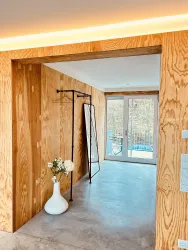 Ein moderner Eingangsbereich mit Holzvertäfelung und einem großen Spiegel. Durch die Glastüren ist ein Blick nach draußen auf einen Pool möglich.