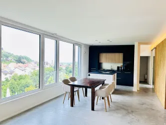 Eine moderne Wohnung mit großen Fenstern und einem Blick auf die Landschaft. Der Essbereich ist mit einem Holztisch und Stühlen ausgestattet.