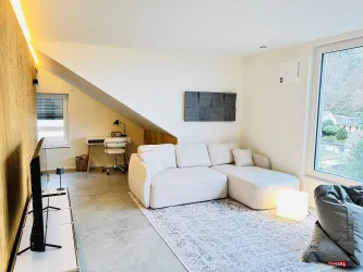 Ein modernes Wohnzimmer mit einem bequemen Sofa und einem großen Fenster. Der Raum hat helle Wände und eine minimalistische Einrichtung.