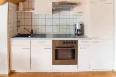 Eine moderne Küchenzeile mit hellen Schränken und grauer Arbeitsplatte. Sie enthält ein Waschbecken, einen Herd und einen Kaffeeautomaten.