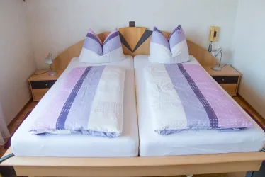 Ein gemütliches Schlafzimmer mit zwei Einzelbetten und bunten Bettwäsche. Neben den Betten befinden sich Nachttische und eine Lampe.