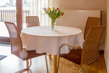 Ein runder Tisch mit einer weißen Tischdecke steht in einem hellen Raum. In der Mitte des Tisches befindet sich eine Vase mit bunten Tulpen.