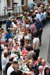 Eine große Gruppe von Menschen sitzt an einem langen Tisch und genießt ein gemeinsames Essen. Die Atmosphäre sieht freundlich und festlich aus.