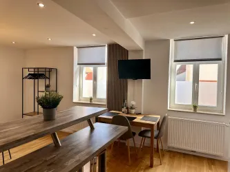 Eine helle Wohnung mit modernen Möbeln. Der Raum hat große Fenster und einen gemütlichen Esstisch.
