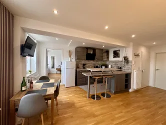 Eine moderne Küche mit Holzfußboden und modernen Möbeln. Es gibt einen Essbereich mit Stühlen und einen Fernseher an der Wand.