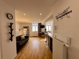 Eine moderne Wohnung mit einer offenen Raumgestaltung. Der Boden ist aus Holz und es gibt eine gemütliche Sitzecke sowie einen Tisch und Stühle.