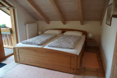 Ein gemütliches Schlafzimmer mit einem Doppelbett aus Holz und zwei Nachttischen. Das Zimmer hat eine Holzdecke und einen Balkon mit Aussicht.
