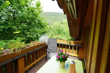 Ein gemütlicher Balkon mit einem Tisch und einem Stuhl. Umgeben von üppigem Grün und einer schönen Aussicht auf die Natur.