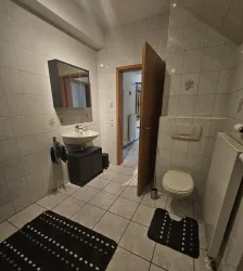 Ein modernes Badezimmer mit weißen Fliesen und einem großen Spiegel. Es gibt eine Toilette, ein Waschbecken und einen Handtuchhalter.