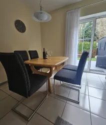 Ein moderner Essbereich mit einem Holztablett und schwarzen Stühlen. Große Fenster bieten einen Blick auf den Außenbereich.