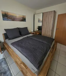 Ein gemütliches Schlafzimmer mit einem großen Holzbett und grauer Bettwäsche. Neben dem Bett steht ein Nachttisch und es gibt einen Holzschrank sowie ein Bild an der Wand.