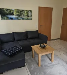 Ein modernes Wohnzimmer mit einem dunkelblauen Sofa und einem holzigen Couchtisch. An der Wand hängt ein Bild einer Landschaft mit einem Fluss und Bäumen.
