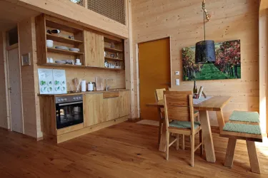 Eine helle, moderne Küche mit Holzregalen und einem Esstisch. Die Wände sind aus Holz, und ein farbenfrohes Bild hängt an der Wand.