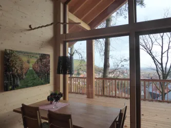 Ein modernes Zimmer mit großen Fenstern, das einen Blick auf die Landschaft bietet. Ein Holztisch und Stühle schaffen eine gemütliche Atmosphäre.