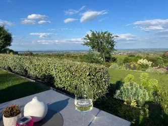 Eine schöne Gartenlandschaft mit Blick auf das Tal. Ein Glas Wein steht auf einem Tisch und der Himmel ist klar und blau.