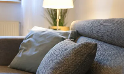 Ein modernes Sofa mit dekorativen Kissen und einer Tischlampe im Hintergrund. Die Einrichtung wirkt gemütlich und einladend.