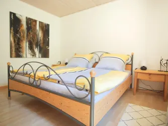 Ein gemütliches Schlafzimmer mit einem großen Bett und gelb-blauen Bettdecken. An der Wand hängt ein modernes Kunstwerk, daneben steht ein Nachttisch.