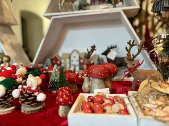 Ein festlicher Weihnachtsmarkt mit einem beleuchteten Weihnachtsbaum. Die Atmosphäre ist gemütlich, mit vielen Menschen, die die Stände besuchen.