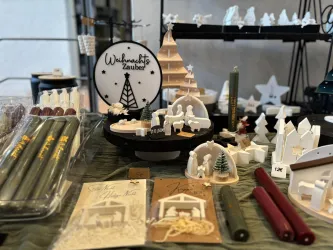 Ein festlich dekorierter Tisch mit Weihnachtsartikeln. Es gibt Kerzen, Holzfiguren und Geschenkkarten, die eine gemütliche Stimmung verbreiten.