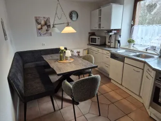 Eine moderne Küche mit einem Esstisch und einer gemütlichen Bank. Das Zimmer hat eine helle Atmosphäre und große Fenster.