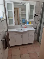 Ein modernes Badezimmer mit einem weißen Waschbecken und einem Spiegel. Der Raum ist hell und freundlich gestaltet.