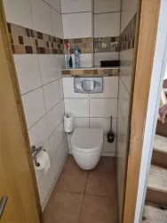 Ein kleines Badezimmer mit einer Toilette und hellen Fliesen. Auf dem Regal sind Toilettenartikel und ein Handtuchhalter sichtbar.