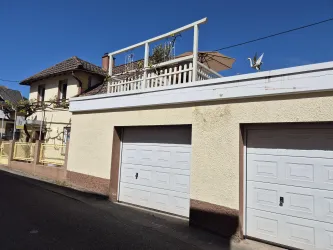Ein Haus mit Garagen und einer Terrasse. Der Himmel ist klar und blau.