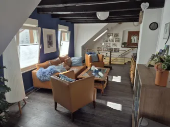 Ein gemütliches Wohnzimmer mit braunen Ledermöbeln und blauen Akzenten. Große Fenster sorgen für viel Tageslicht und eine einladende Atmosphäre.