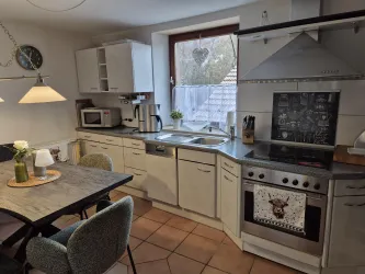 Eine moderne Küche mit hellen Schränken und einem Esstisch. Durch das Fenster fällt Licht auf die Arbeitsfläche.