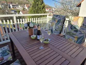 Ein schöner Tisch auf einer Terrasse mit Stühlen im tropischen Design. Auf dem Tisch stehen Blumen, zwei Gläser Sekt und Snacks.