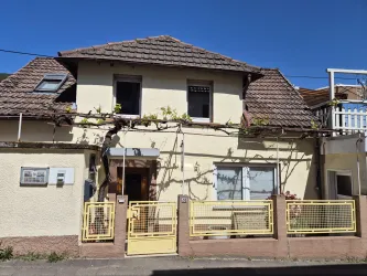 Ein charmantes Haus mit einem gepflasterten Eingang und einem gelben Zaun. Die Fassade ist mit Pflanzen verziert und der Himmel ist klar blau.